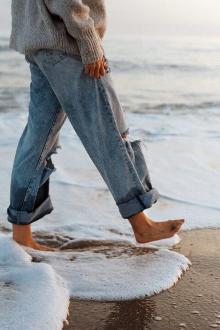 A person walking on the beach with their feet in water.