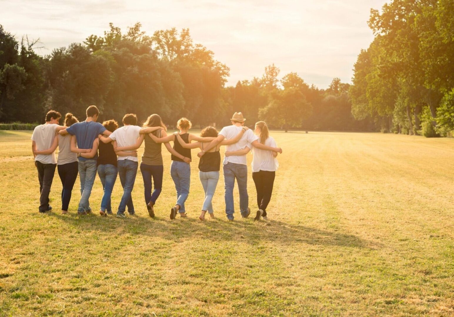 A group of people standing in the grass with their hands around each other.